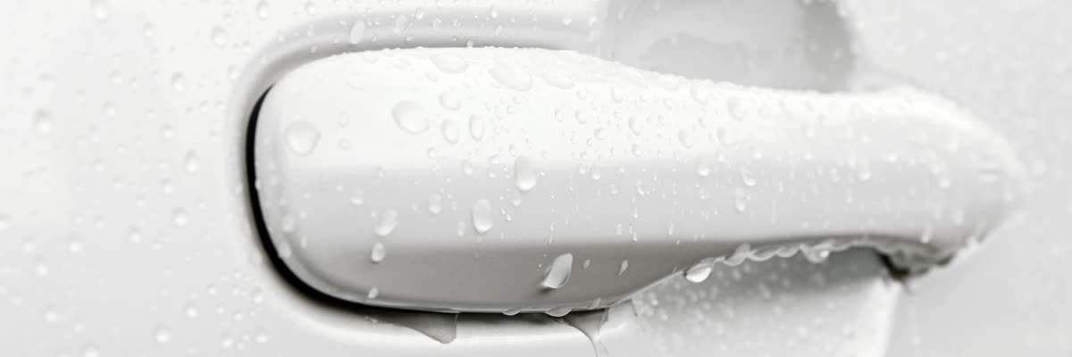 Water standing in tight beads on the painted door and handle of a white car