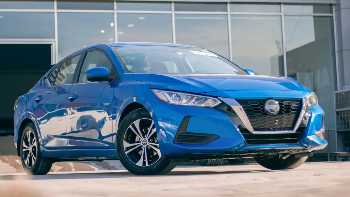 A blue compact sedan parked outside a bright glass and steel building