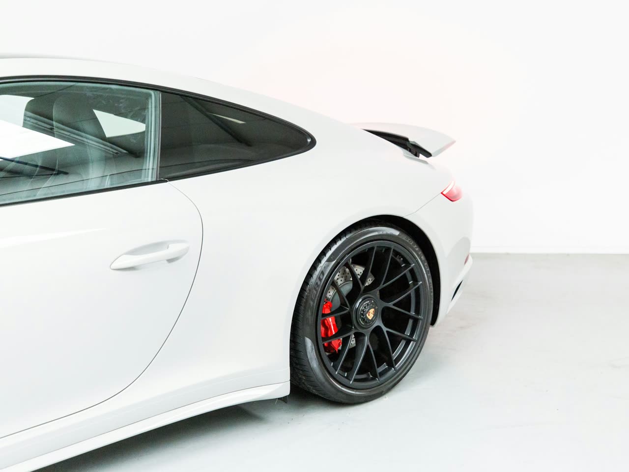 A white Porsche in a bright, high-key detailing studio with a polished concrete floor, lit evenly under 5000K light